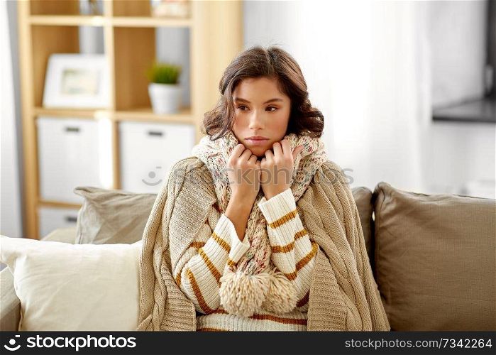 people, health and cold concept - sad sick woman in blanket and scarf at home. sad sick woman in blanket and scarf at home