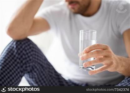 people, health and hydration concept - close up of unhealthy man suffering from hangover with glass of water in morning. close up of sick man with glass of water