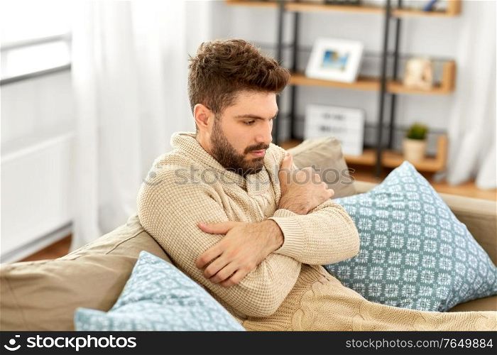 people, health and medicine concept - sad sick man in blanket having fever at home. sad sick man in blanket having fever at home