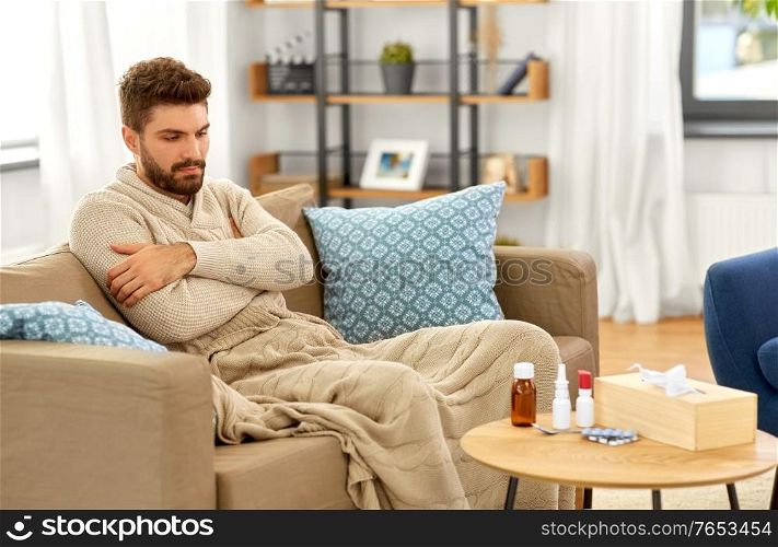 people, health and medicine concept - sad sick man in blanket with drugs and box of paper tissues at home. sad sick man in blanket with medicine at home