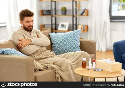 people, health and medicine concept - sad sick man in blanket with drugs and box of paper tissues at home. sad sick man in blanket with medicine at home