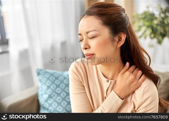 people, health and problem concept - tired asian woman suffering from ache in neck at home. asian woman suffering from ache in neck at home