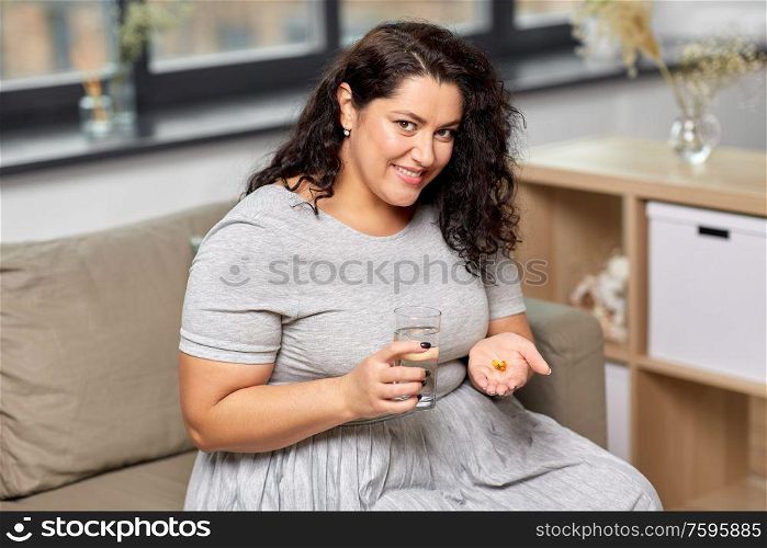 people, health and treatment concept - young woman taking cod liver oil pills with water at home. woman with cod liver oil pills and water at home