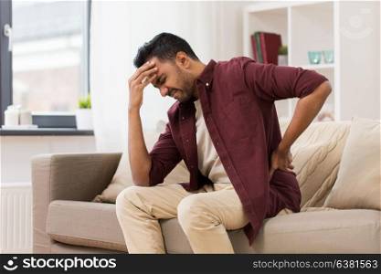 people, health care and problem concept - unhappy man suffering from pain in back or reins at home. unhappy man suffering from backache at home
