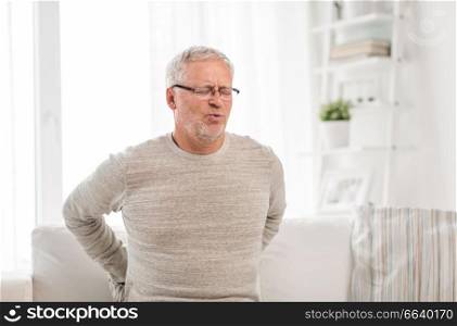 people, health care and problem concept - unhappy senior man suffering from pain in back or reins at home. unhappy senior man suffering from backache at home
