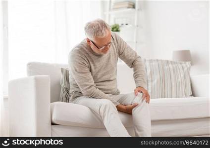 people, health care and problem concept - unhappy senior man suffering from knee ache at home. senior man suffering from knee ache at home