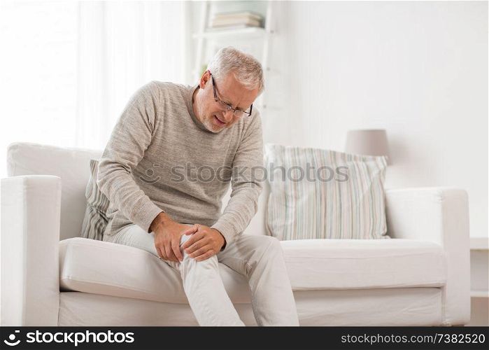 people, health care and problem concept - unhappy senior man suffering from knee ache at home. senior man suffering from knee ache at home