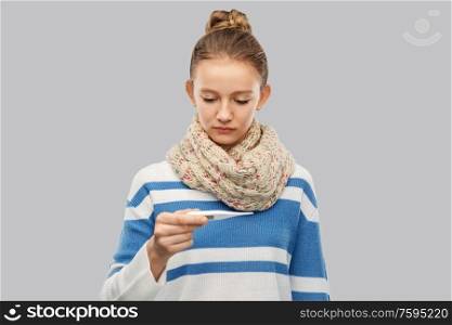 people, health problem and fever concept - sad sick teenage girl in scarf measuring temperature by thermometer over grey background. sick teenage girl in scarf measuring temperature