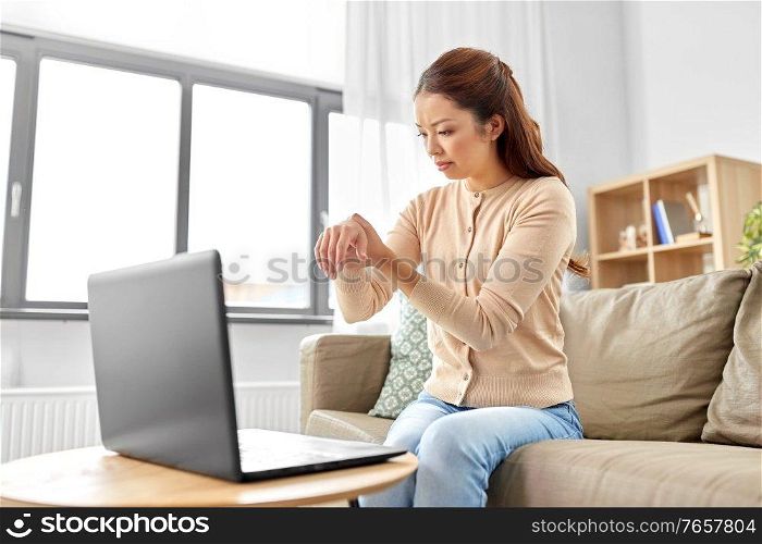 people, health problem and remote job concept - unhappy asian woman with laptop suffering from ache in hand or carpal tunnel syndrome at home office. asian woman suffering from ache in hand at home