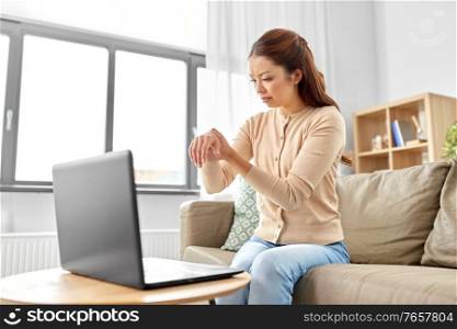 people, health problem and remote job concept - unhappy asian woman with laptop suffering from ache in hand or carpal tunnel syndrome at home office. asian woman suffering from ache in hand at home