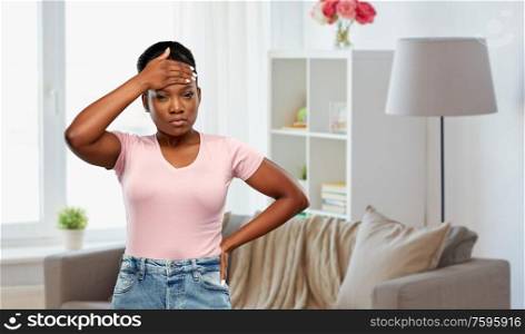 people, health problem and stress concept - unhappy african american woman suffering from headache or fever over home room background. african american woman having headache or fever