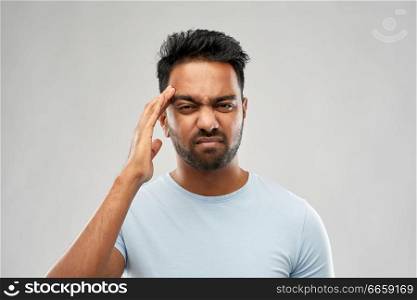 people, health problem and stress concept - unhappy indian man suffering from headache over grey background. unhappy indian man suffering from headache