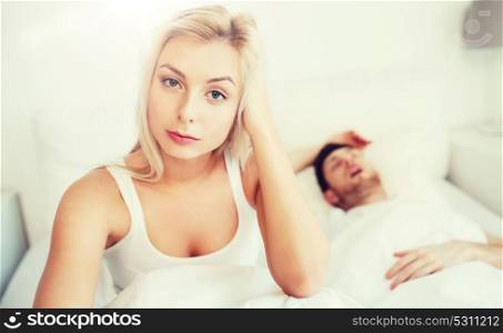 people, health, sleep disorder concept - couple in bed at home, man snoring and young woman suffering from insomnia. awake woman having insomnia in bed