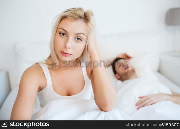 people, health, sleep disorder concept - couple in bed at home, man snoring and young woman suffering from insomnia