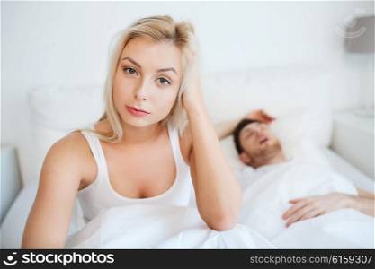 people, health, sleep disorder concept - couple in bed at home, man snoring and young woman suffering from insomnia