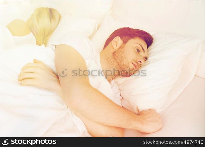 people, health, sleep disorder concept - couple lying back to back in bed at home and young man suffering from insomnia
