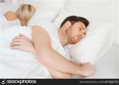 people, health, sleep disorder concept - couple lying back to back in bed at home and young man suffering from insomnia