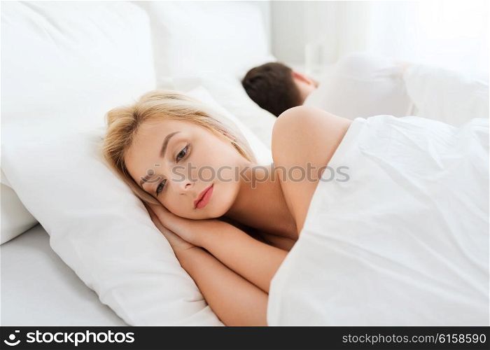 people, health, sleep disorder concept - couple lying back to back in bed at home and young woman suffering from insomnia