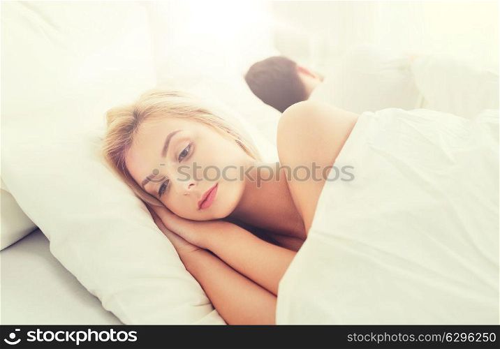 people, health, sleep disorder concept - couple lying back to back in bed at home and young woman suffering from insomnia. young woman suffering from insomnia