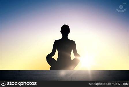 people, health, wellness and meditation concept - woman meditating in yoga lotus pose on stairs over sun light background