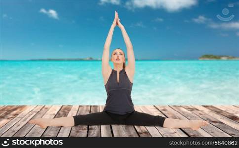 people, health, wellness and sport concept - happy young woman in yoga pose on wooden floor over sea and blue sky background