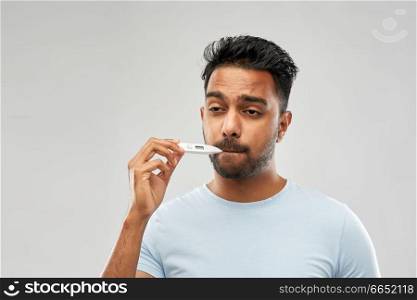 people, healthcare and fever concept - unhealthy indian man measuring oral temperature by thermometer over grey background. man measuring oral temperature by thermometer