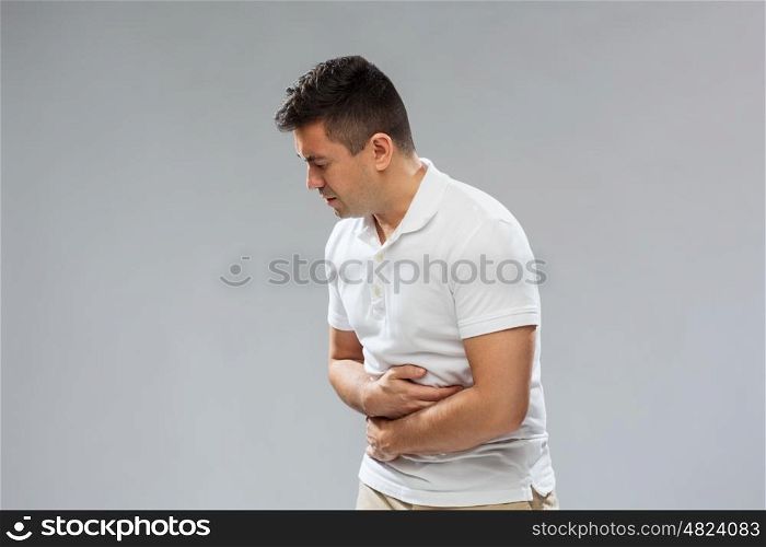 people, healthcare and health problem concept - unhappy man suffering from stomach ache over gray background
