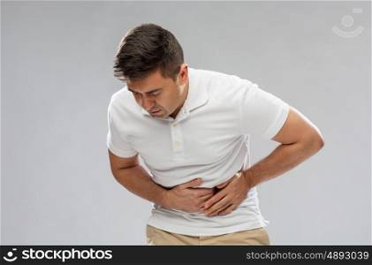 people, healthcare and health problem concept - unhappy man suffering from stomach ache over gray background
