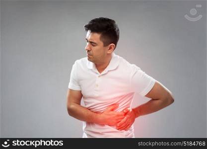 people, healthcare and health problem concept - unhappy man suffering from stomach ache over gray background. unhappy man suffering from stomach ache