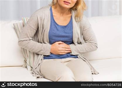 people, healthcare and problem concept - close up of unhappy woman suffering from stomach ache at home
