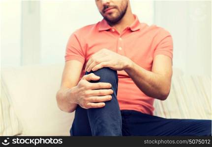 people, healthcare and problem concept - close up of young man suffering from pain in leg or knee at home. close up of man suffering from pain in leg at home