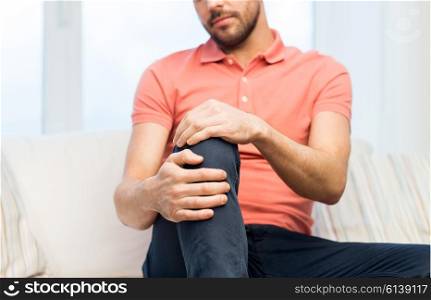 people, healthcare and problem concept - close up of young man suffering from pain in leg or knee at home