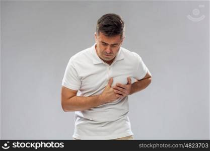 people, healthcare and problem concept - unhappy man suffering from heart ache over gray background