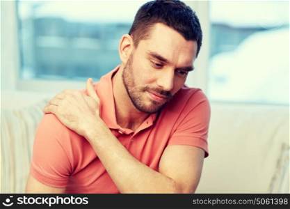 people, healthcare and problem concept - unhappy man suffering from neck or shoulder pain at home. unhappy man suffering from neck pain at home