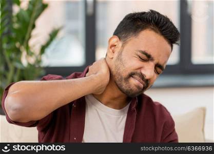 people, healthcare and problem concept - unhappy man suffering from neck pain at home. unhappy man suffering from neck pain at home