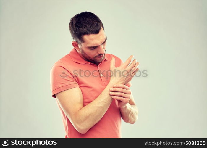 people, healthcare and problem concept - unhappy man suffering from pain in hand over gray background. unhappy man suffering from pain in hand