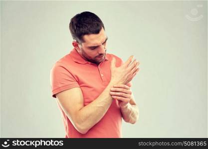 people, healthcare and problem concept - unhappy man suffering from pain in hand over gray background. unhappy man suffering from pain in hand