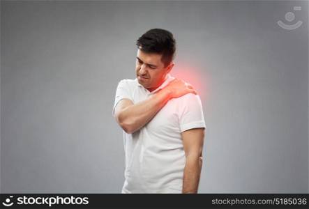 people, healthcare and problem concept - unhappy man suffering from pain in shoulder over gray background. unhappy man suffering from pain in shoulder