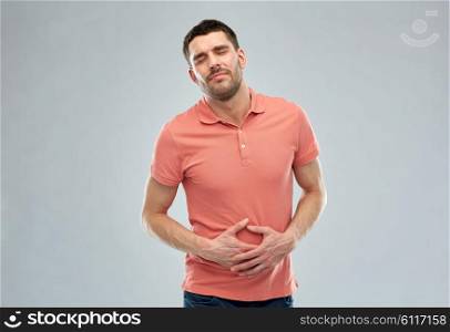 people, healthcare and problem concept - unhappy man suffering from stomach ache over gray background