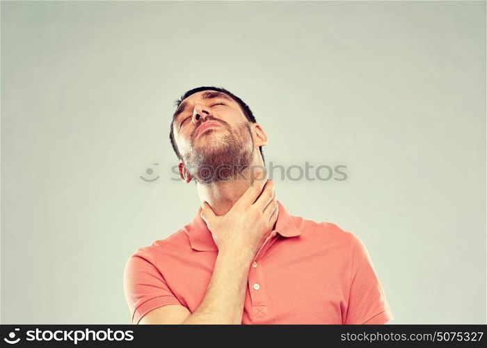 people, healthcare and problem concept - unhappy man touching his neck and suffering from throat pain over gray background. man touching neck and suffering from throat pain