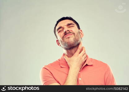 people, healthcare and problem concept - unhappy man touching his neck and suffering from throat pain over gray background. man touching neck and suffering from throat pain