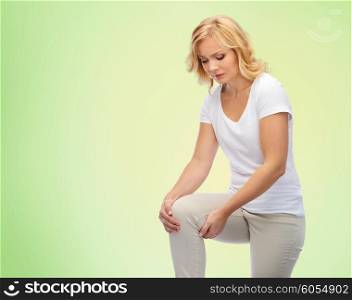 people, healthcare and problem concept - unhappy middle aged woman suffering from pain in leg or knee at home over green natural background