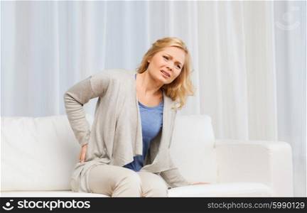 people, healthcare and problem concept - unhappy woman suffering from pain in back or reins at home