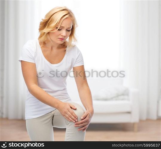 people, healthcare and problem concept - unhappy woman suffering from pain in leg over living room background