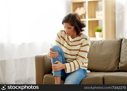 people, healthcare and problem concept - unhappy young woman suffering from pain in leg at home. unhappy woman suffering from pain in leg at home