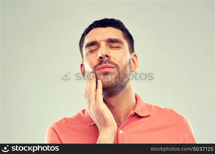 people, healthcare, dentistry and problem concept - unhappy man suffering from toothache over gray background. unhappy man suffering from toothache