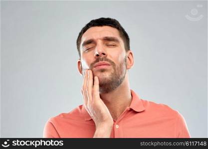 people, healthcare, dentistry and problem concept - unhappy man suffering from toothache over gray background