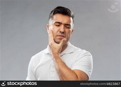 people, healthcare, dentistry and problem concept - unhappy man suffering toothache over gray background