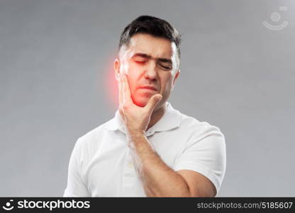 people, healthcare, dentistry and problem concept - unhappy man suffering toothache over gray background. unhappy man suffering toothache