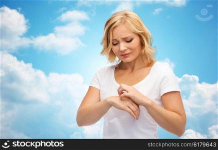 people, healthcare, dermatology, allergy and health problem concept - unhappy woman suffering from hand inch over blue sky and clouds background